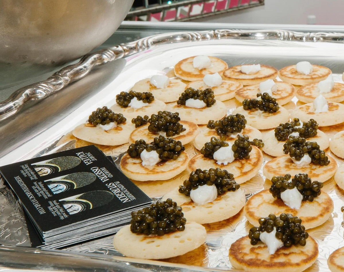 An Appetizer platter with Meredith Marks' caviar on blinis, topped with cream, served on a silver tray with brochures.