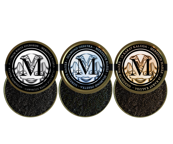 Trio of Meredith Marks caviar tins - Platinum White Sturgeon, Diamond Ossetra, and 24 Karat Kaluga - opened to show glossy black pearls.